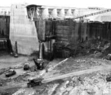 An old black and white photo of a crane building a dam.