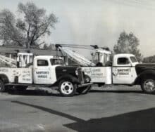 A black and white photo of two tow trucks with a crane.